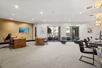 A woman is sitting at a desk in a modern office with a brick wall behind her.