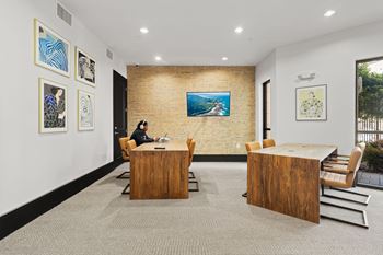 A woman is sitting at a desk in a room with a brick wall and framed pictures on the wall.