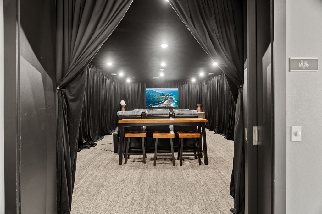 A conference room with a long table and chairs, a screen at the end, and curtains on the sides.