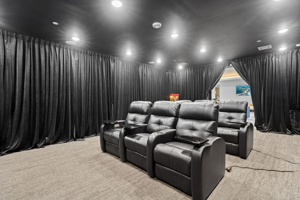 A row of black leather recliner chairs are lined up in a room with black curtains on the sides.