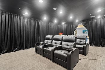 A row of black leather recliner chairs are lined up in a room with black curtains on the sides.