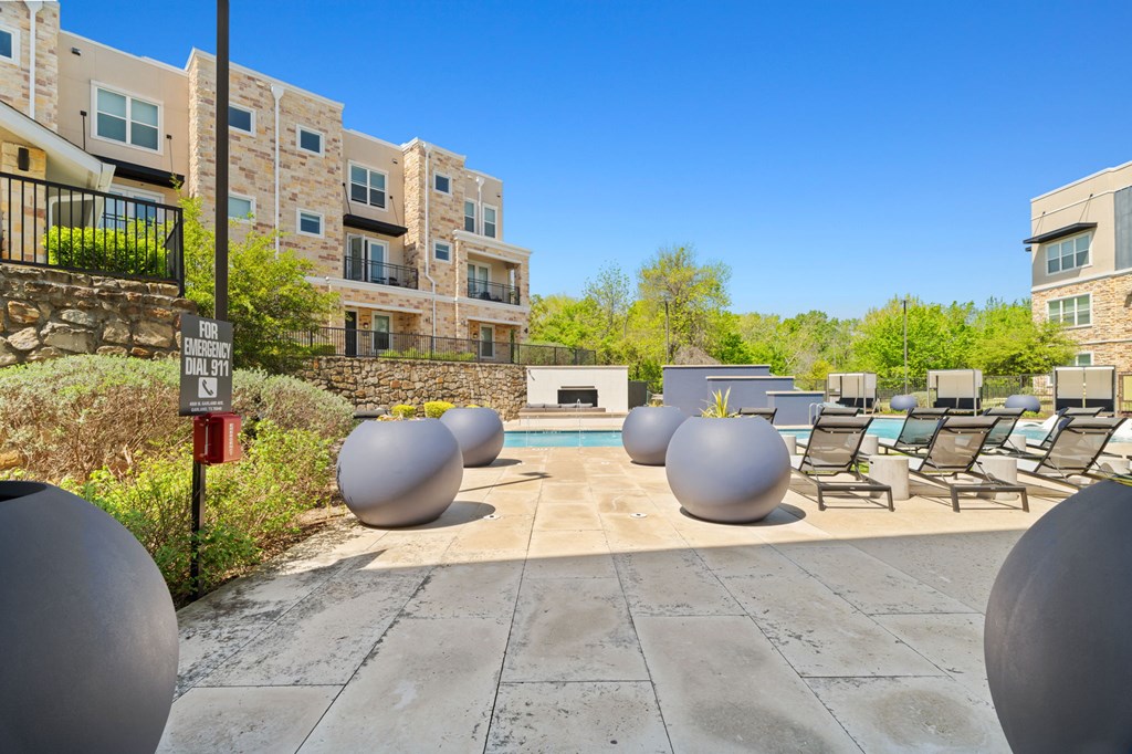A pool surrounded by large grey balls and chairs in front of apartment buildings.