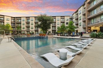 A swimming pool surrounded by lounge chairs and apartment buildings.