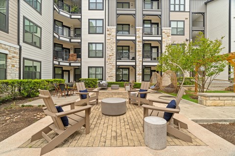 A patio with wooden chairs and a table in front of apartment buildings.