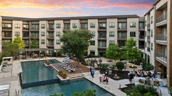 A large swimming pool is surrounded by a patio with lounge chairs and umbrellas.