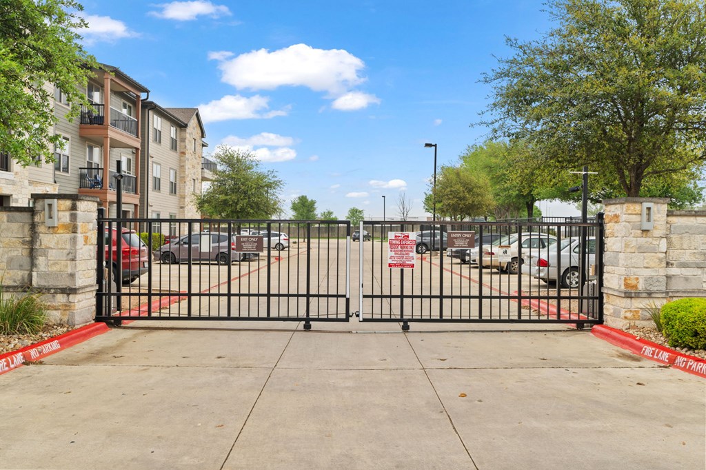 A black gate with a red sign on it in front of a parking lot.
