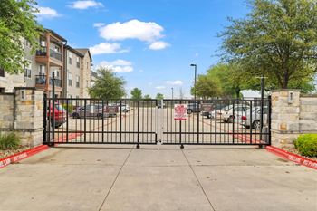 A black gate with a red sign on it in front of a parking lot.