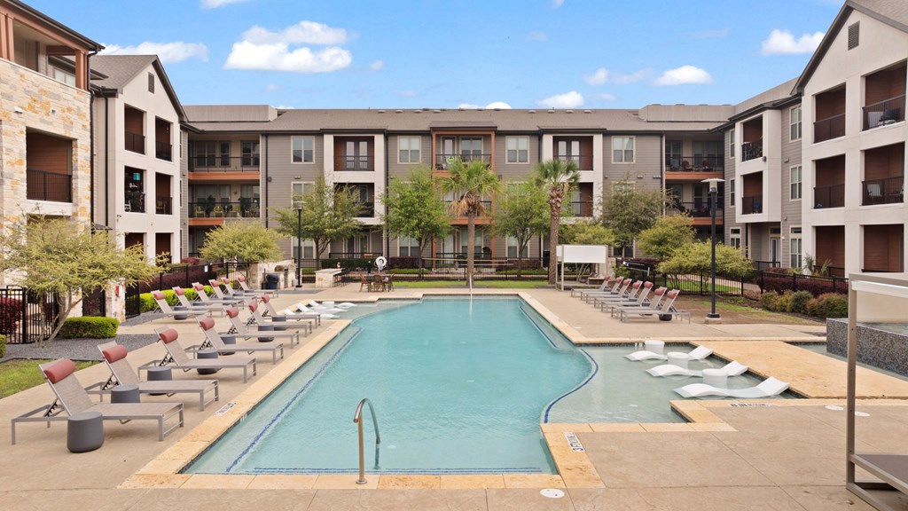 A large swimming pool surrounded by lounge chairs and apartment buildings.