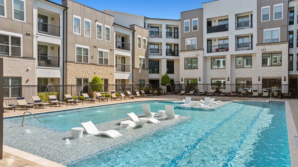 A large swimming pool with lounge chairs in front of apartment buildings.