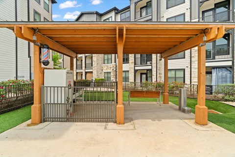 A wooden pergola is in front of a building with a gate.