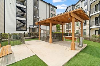 A wooden pavilion is surrounded by a grassy area and apartment buildings.