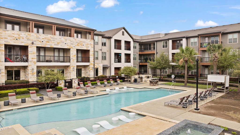 A large swimming pool surrounded by lounge chairs and apartment buildings.