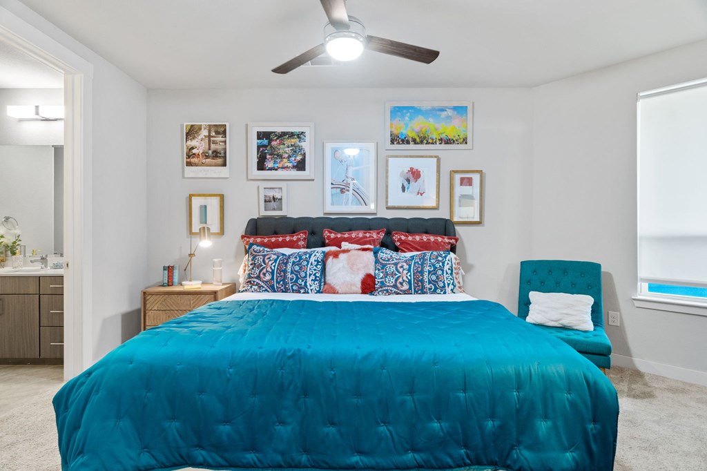 A bedroom with a blue bedspread and a ceiling fan.
