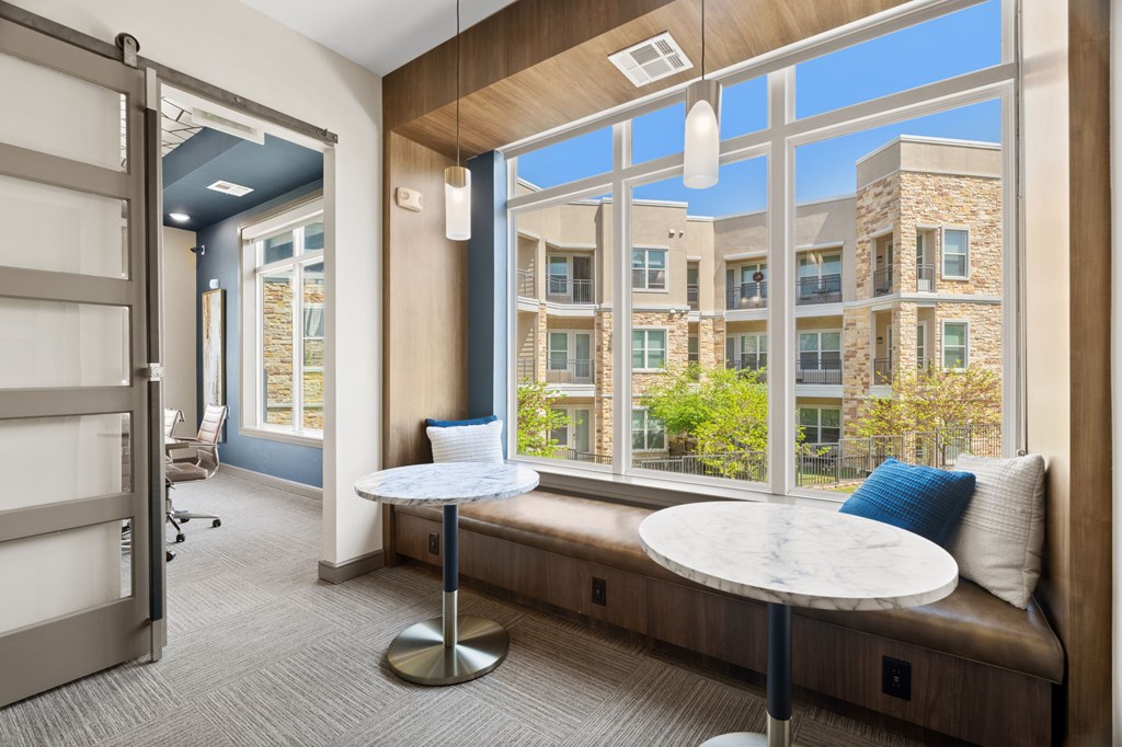 A room with a table and a bench with a view of a building outside.