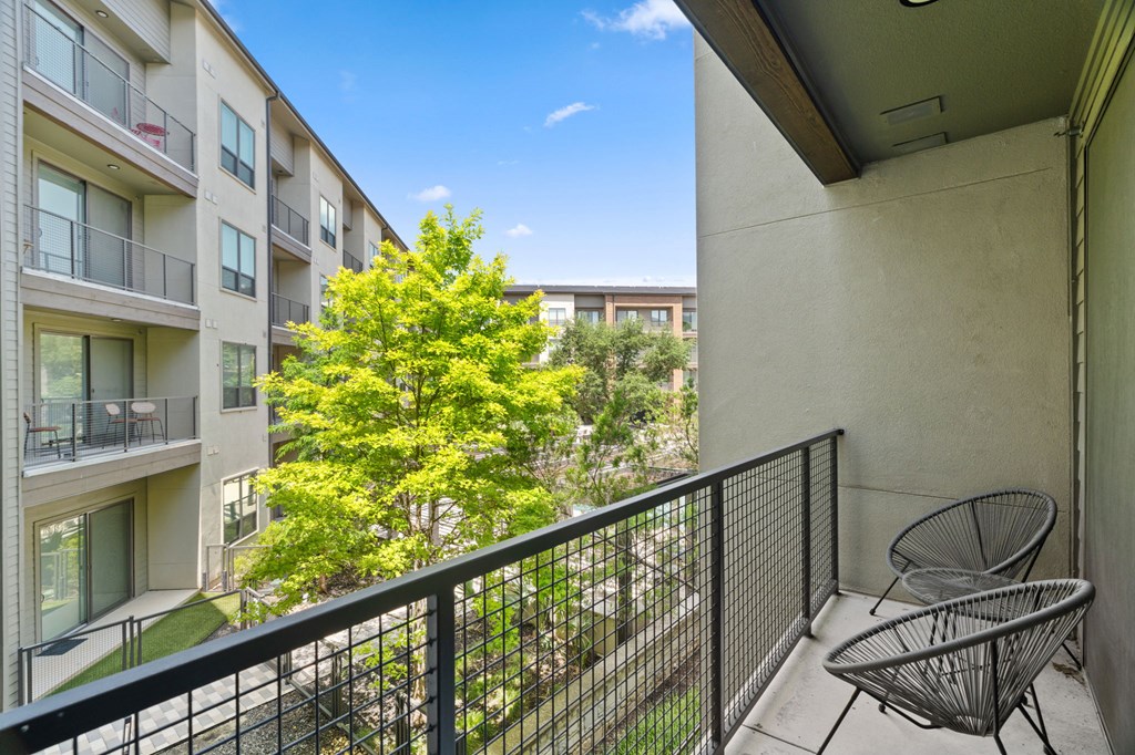 A balcony with a chair and a tree in the background.