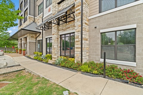 A building with a grey and brown facade has a black railing and a black awning.