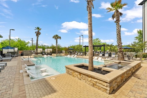 A pool surrounded by palm trees and a stone wall.