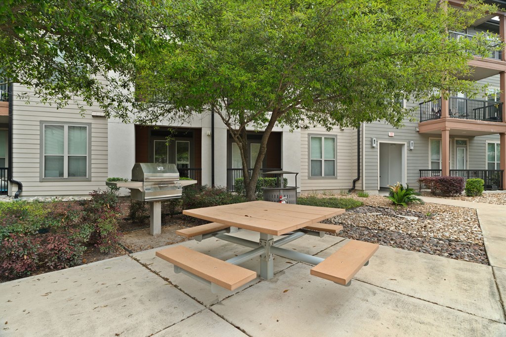 A wooden picnic table is in the middle of a concrete patio.
