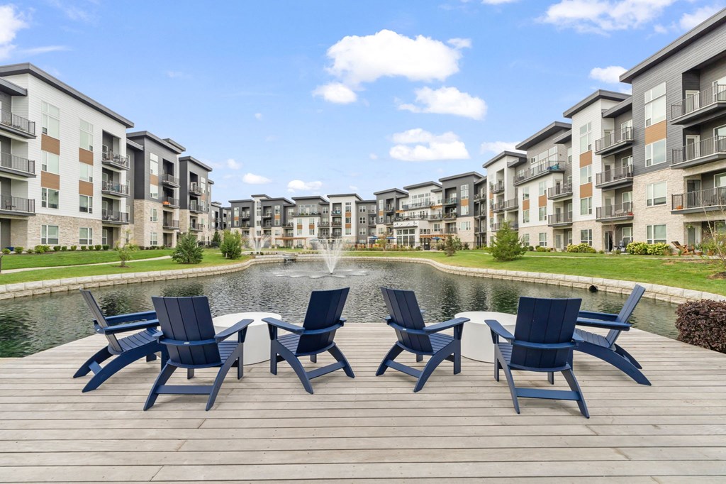 an outdoor patio with blue chairs and a pond in front of an apartment building