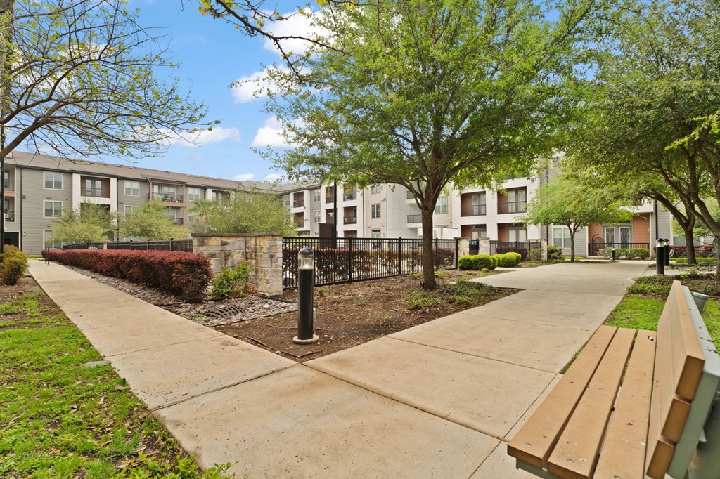 A park area with benches and a fence in front of apartment buildings.