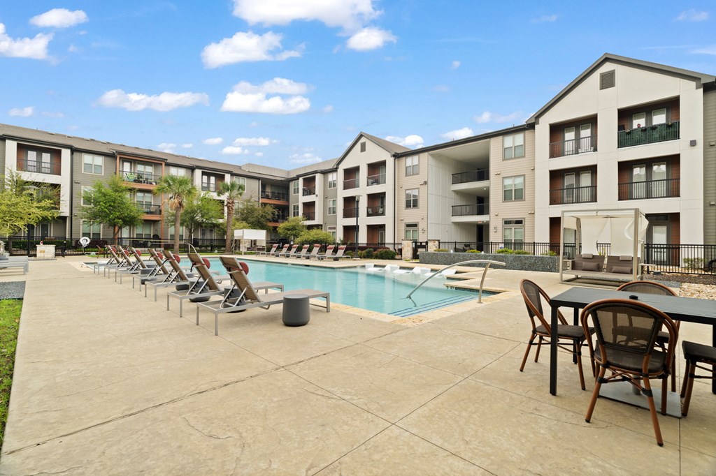 A pool area with chairs and tables in front of apartment buildings.
