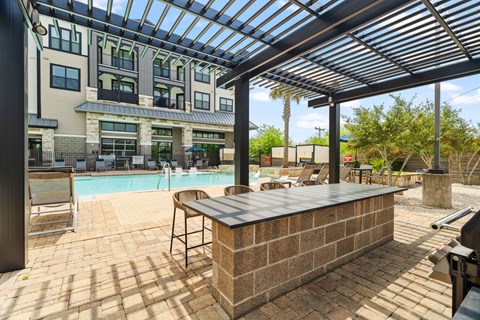 A pool area with a bar and chairs under a roof.