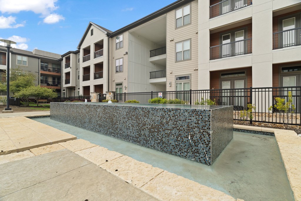A concrete planter with a black fence in front of apartment buildings.