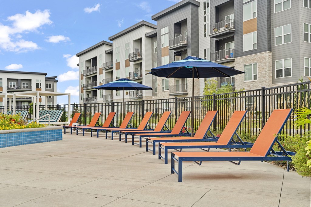 an outdoor lounge area with chairs and umbrellas in front of an apartment building
