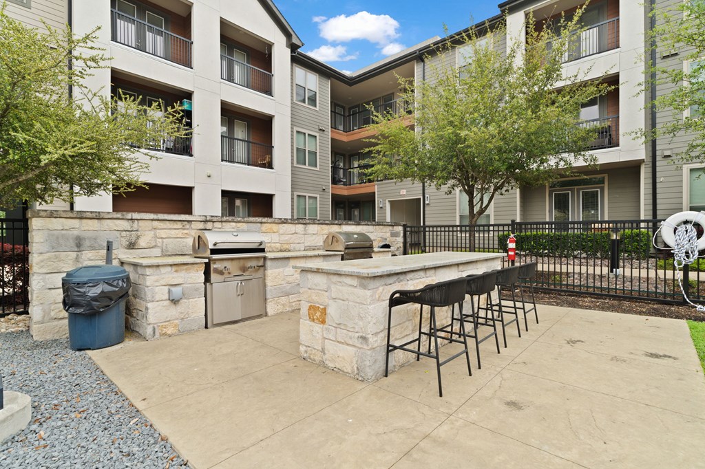 A patio area with a bar and chairs is surrounded by a black fence.