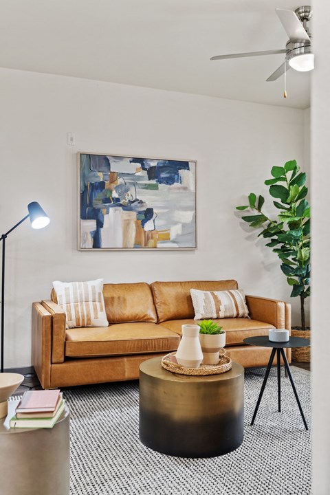 A living room with a brown couch, a round coffee table, and a painting on the wall.