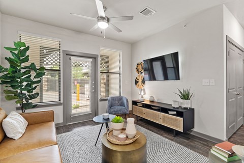 A living room with a brown leather couch, a round coffee table, and a ceiling fan.