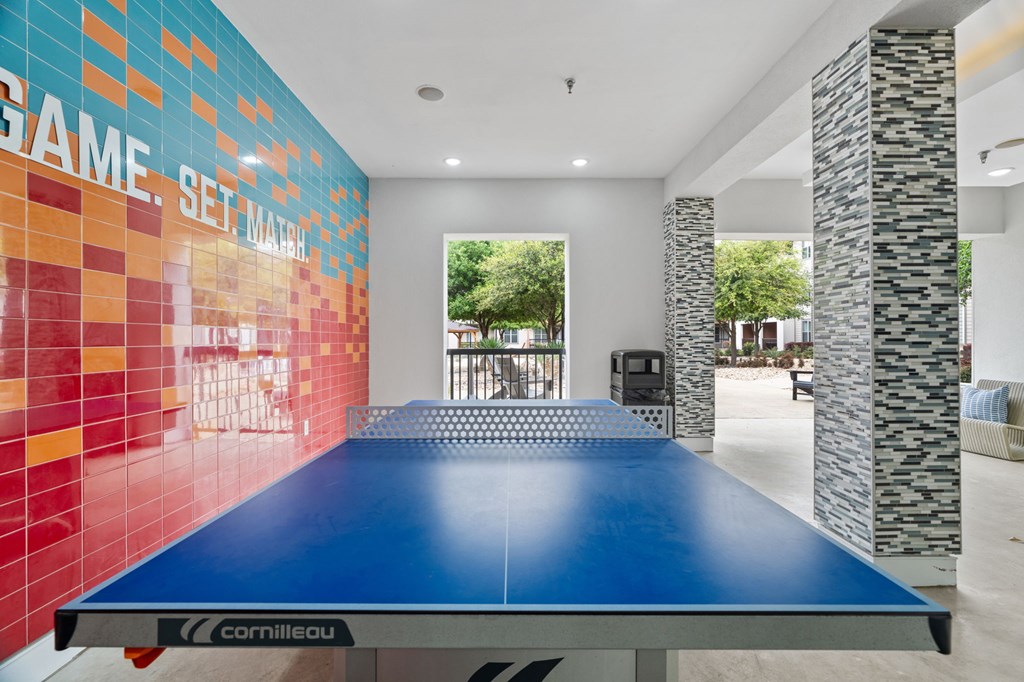 A blue cornilleau table tennis table in a room with a tiled wall.