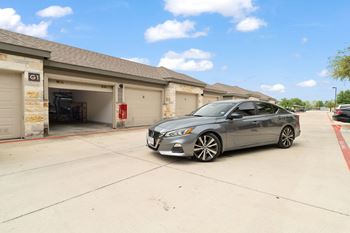 A grey car is parked in front of a garage.