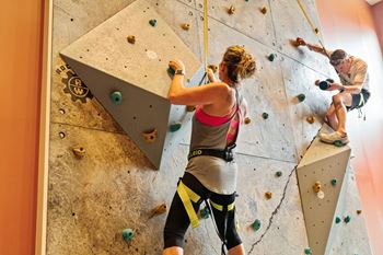 a woman climbing a rock wall with a man on a climbing rope