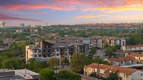 A cityscape with buildings and houses under a pink and blue sky.