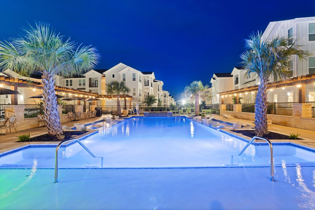 A swimming pool surrounded by palm trees and lit up at night.