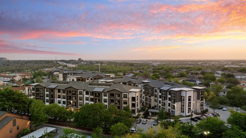 A sunset view of apartment buildings with cars parked in front.
