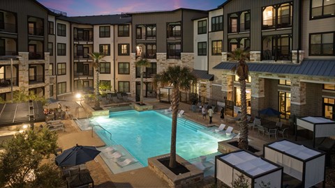 A swimming pool surrounded by a patio with chairs and umbrellas at a resort.