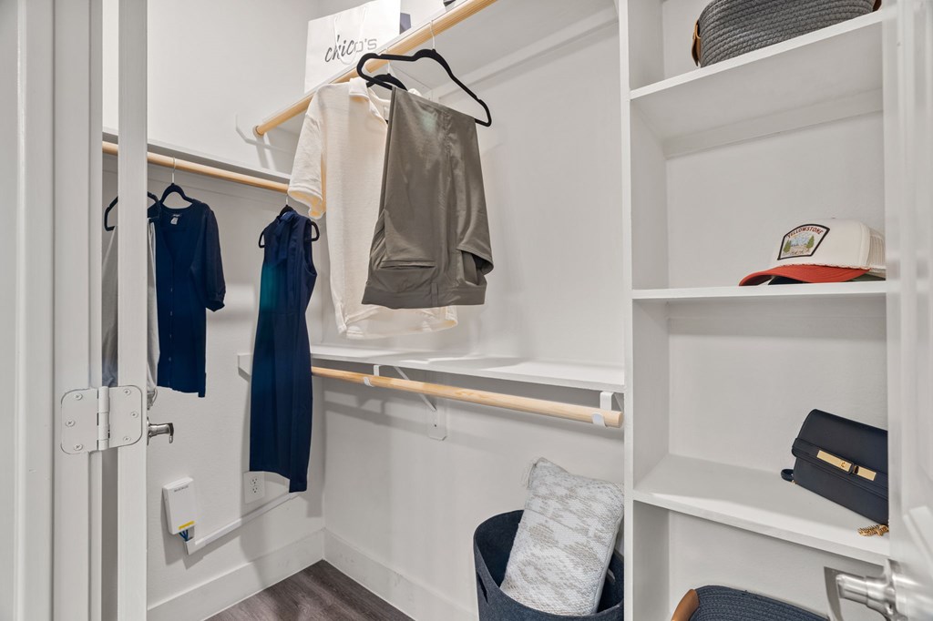 A white closet with clothes hanging and a bag on the shelf.