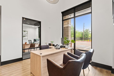 A room with a desk and chairs with a view of a parking lot outside.