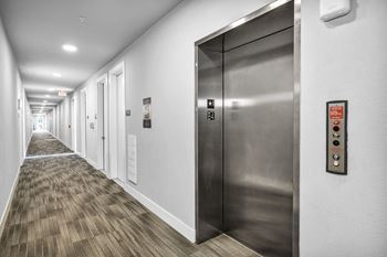 a long corridor with elevators and doors on the left and a hallway on the right