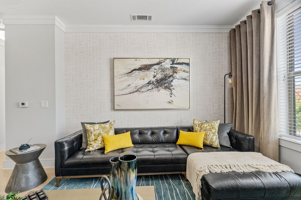 A living room with a black leather couch and a large abstract painting above it.