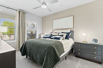 A bedroom with a bed, nightstand, and a window with blinds.