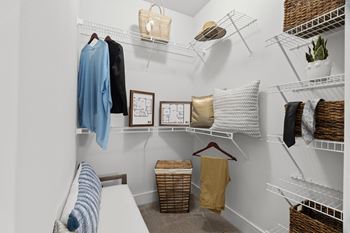 A white closet with clothes and baskets on the shelves.