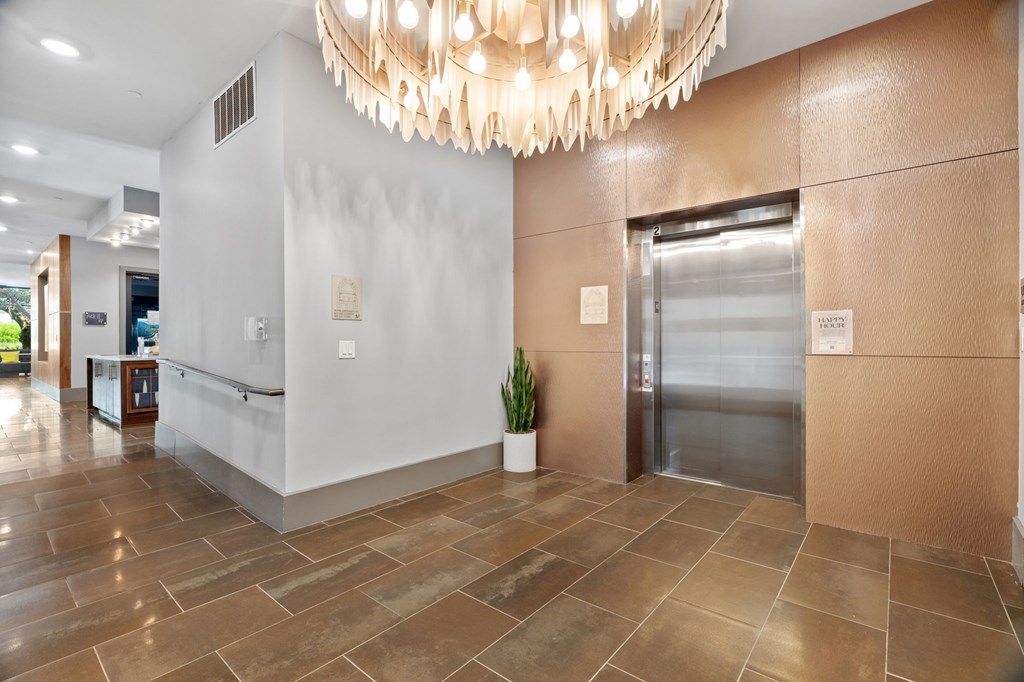 A large, modern chandelier hangs over a reception desk in a well-lit hallway.