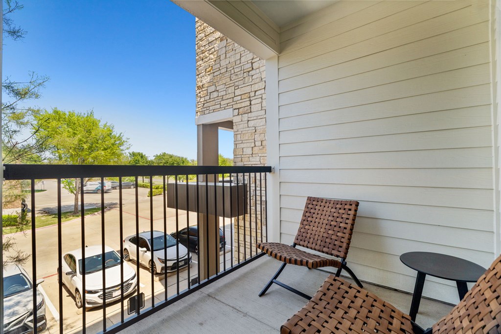 A balcony with a table and two chairs overlooks a parking lot.