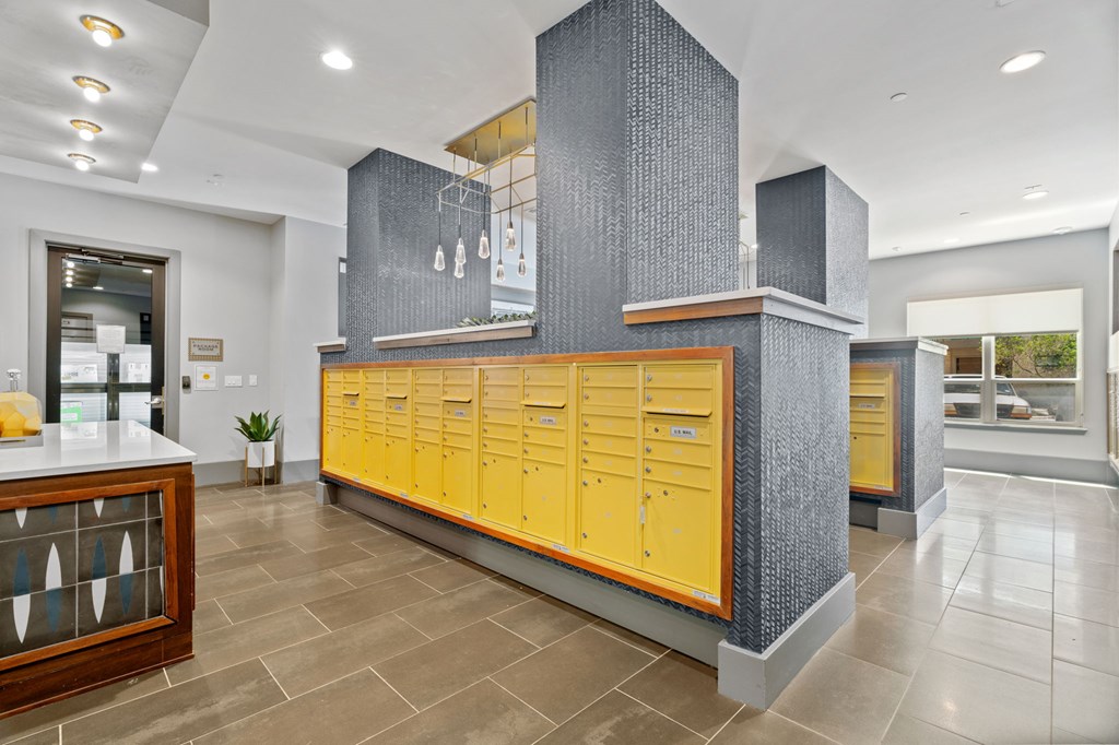 A row of yellow lockers are in a room with a grey column and a counter.