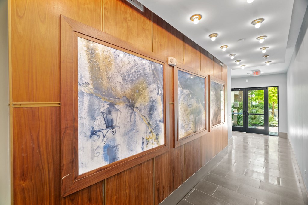 A hallway with a large painting on the wall and a glass door at the end.