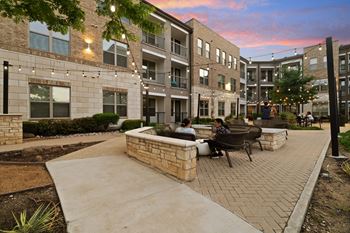 A courtyard with people sitting on a bench and a brick wall.