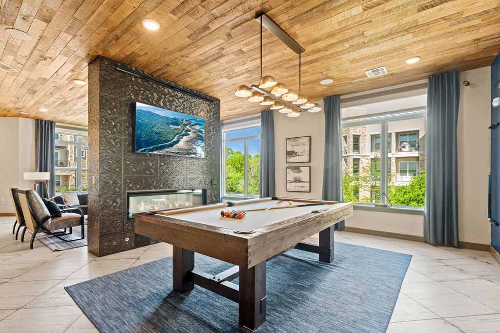 A billiard table is in the middle of a room with a fireplace and a TV above it.
